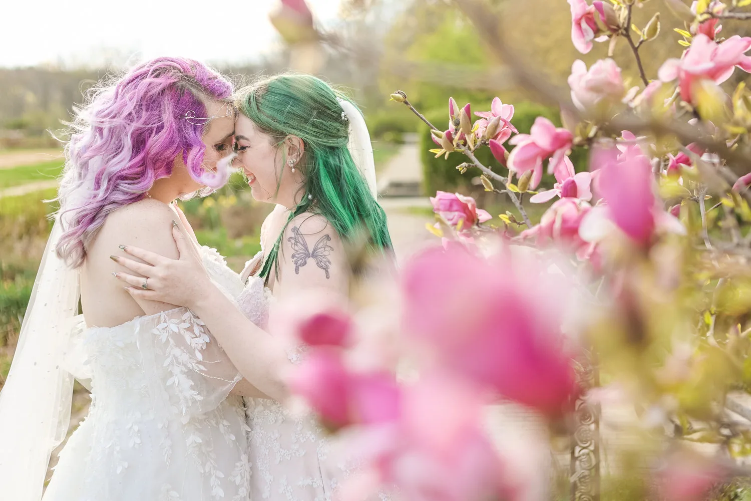 Two brides kissing among pink flowers.