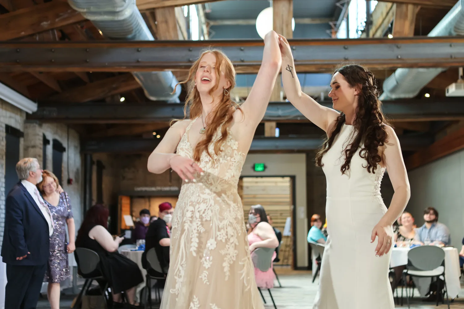 Two brides celebrating with raised hands at their reception.