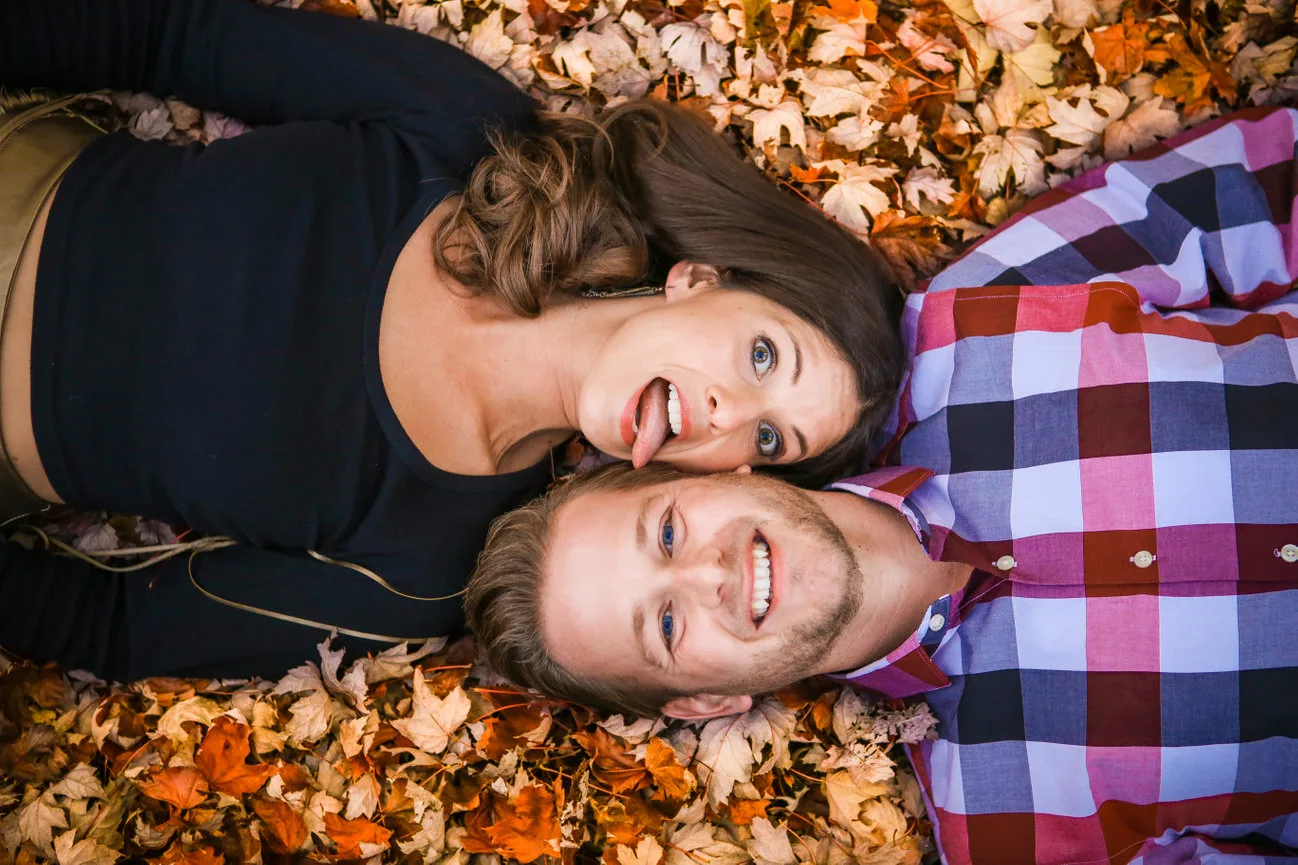 An engaged couple lying together in autumn leaves.